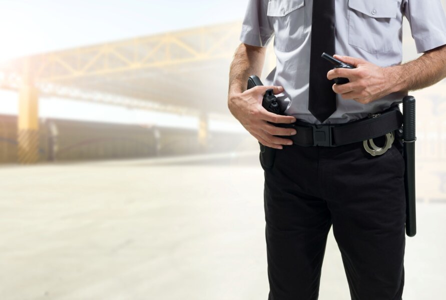 An armed security guard places his hand on his holstered weapon.