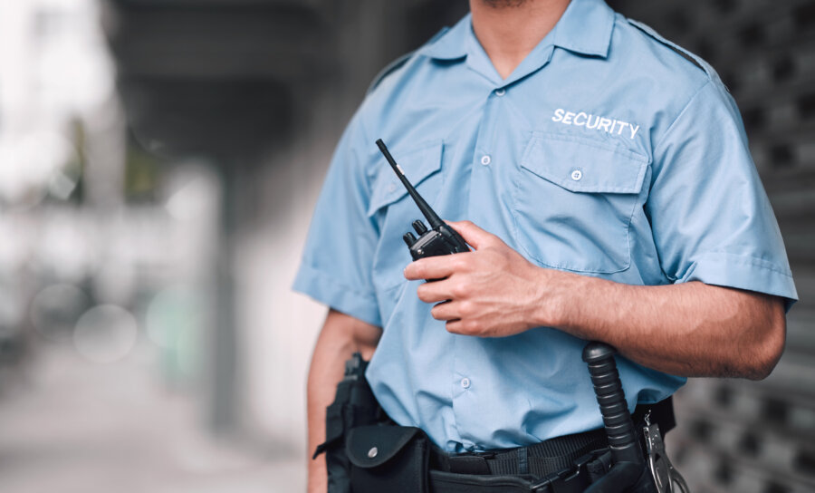 Security officer in uniform holding a two-way radio at a commercial property.